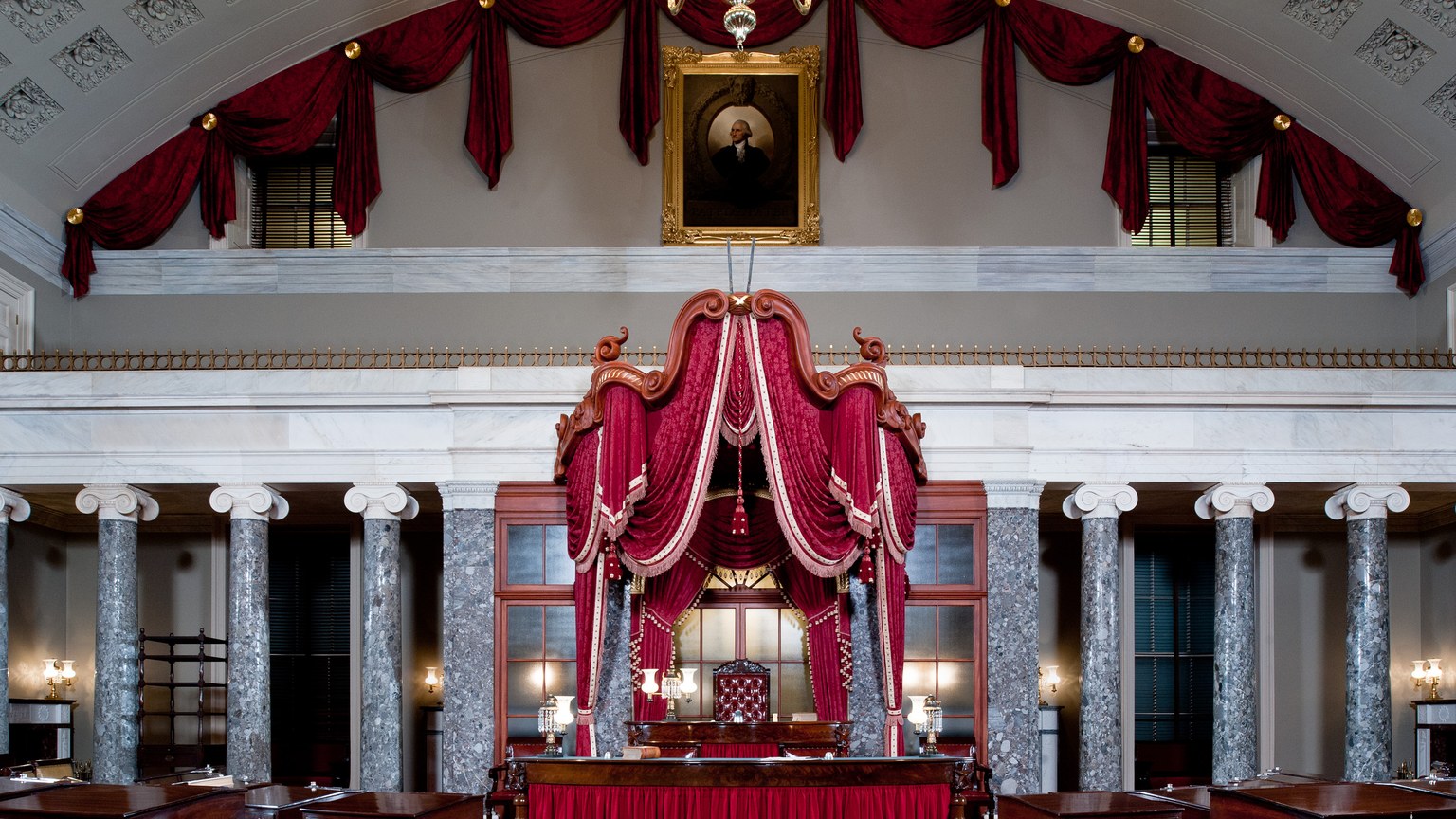 Old Senate Chamber in the U.S. Capitol with red canopy, marble columns, and Washington portrait