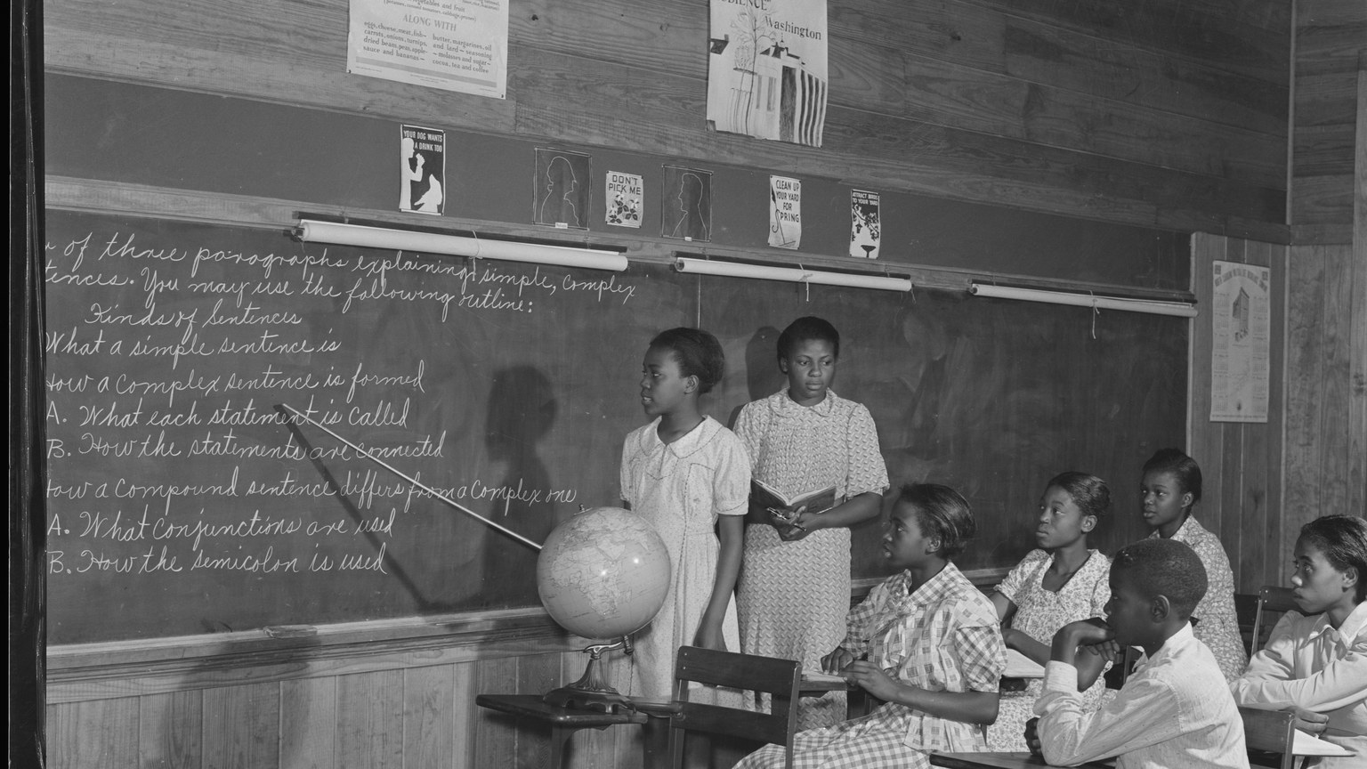 Historic photograph of students at desks during an English classroom lesson with a blackboard outline