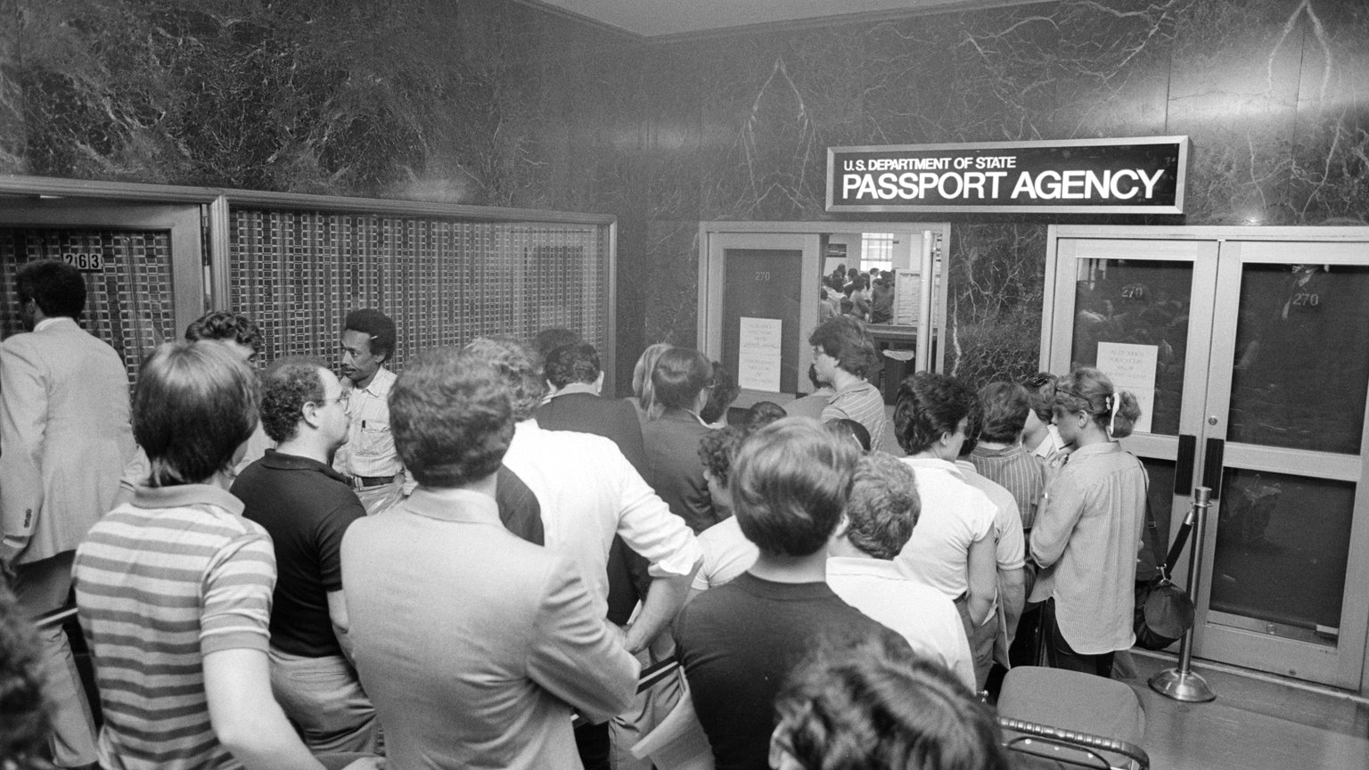 A crowd of people waiting in line outside a U.S. Department of State Passport Agency office in 1983