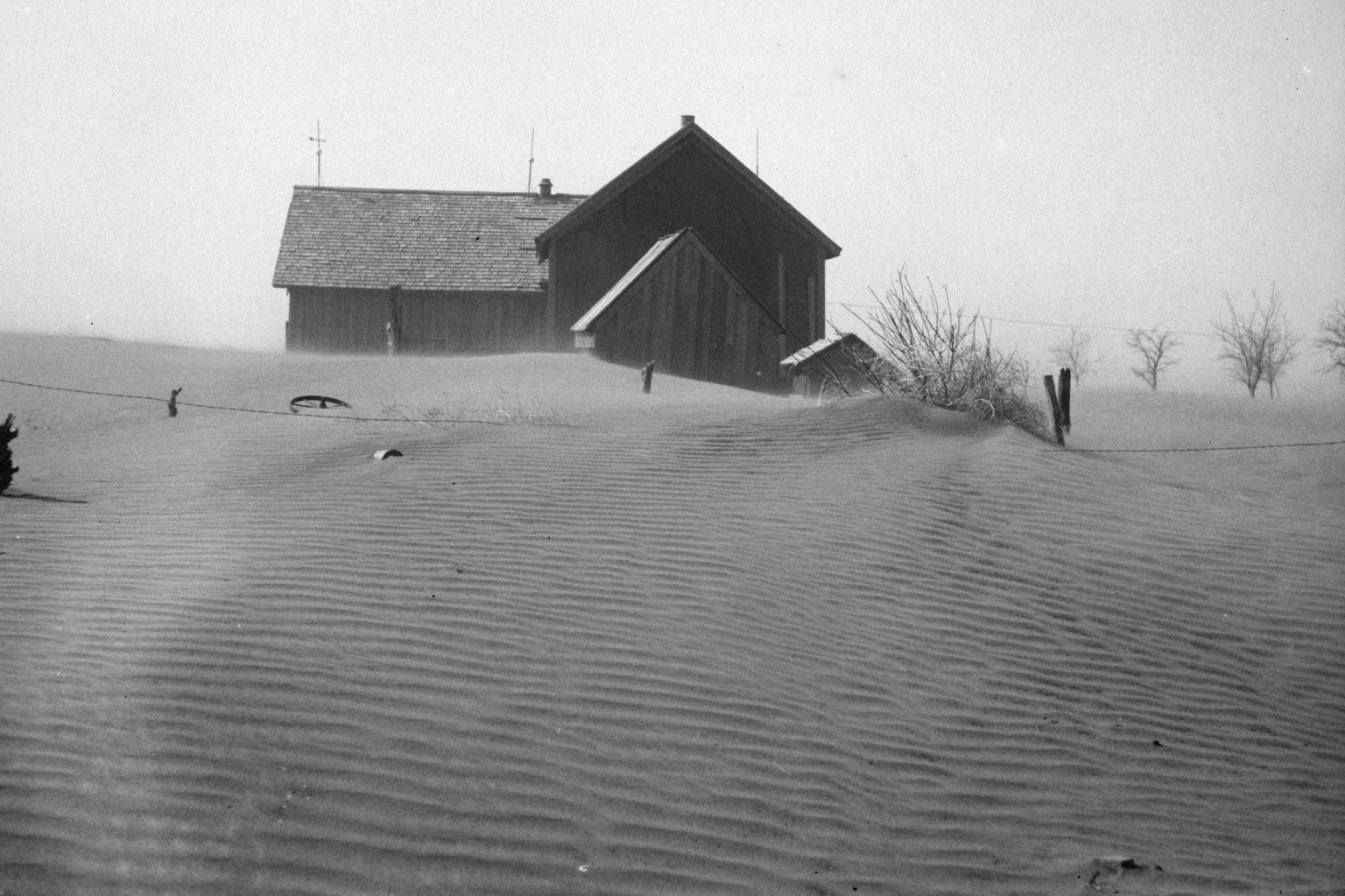 A farmhouse and barn in Cimarron County, Oklahoma, half buried by rippled drifts of dust in a 1936 photograph from the Dust Bowl years