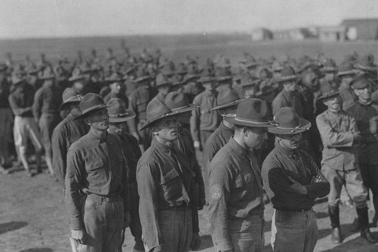 Men in World War I army uniforms and campaign hats stand in line, waiting to be questioned by a naturalization examiner, June 13, 1918