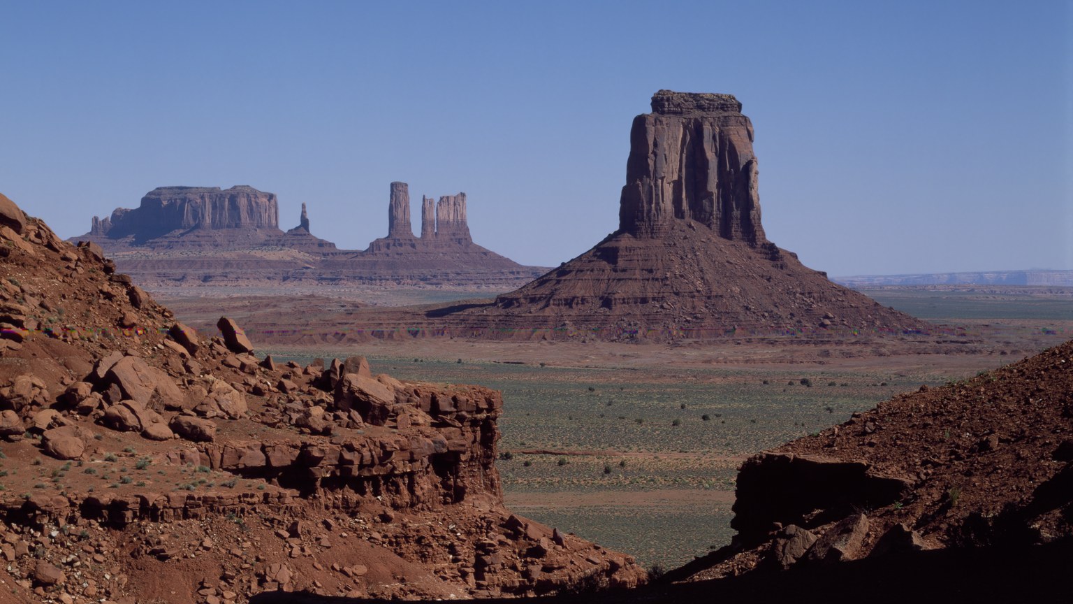 Red sandstone buttes rising from the desert floor at Monument Valley Navajo Tribal Park under a clear blue sky