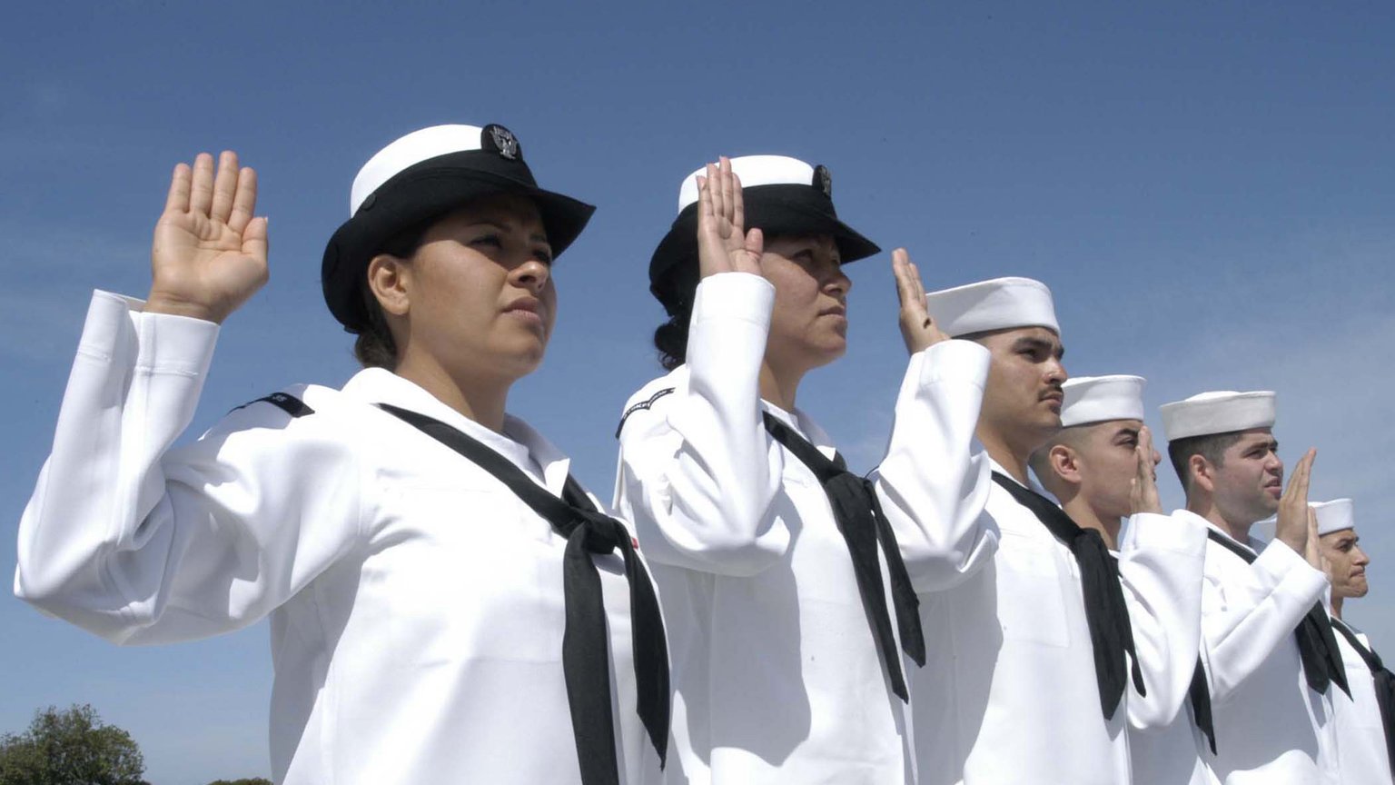 U.S. Navy sailors in white uniforms raise their right hands to take the oath of citizenship at an outdoor naturalization ceremony in San Diego