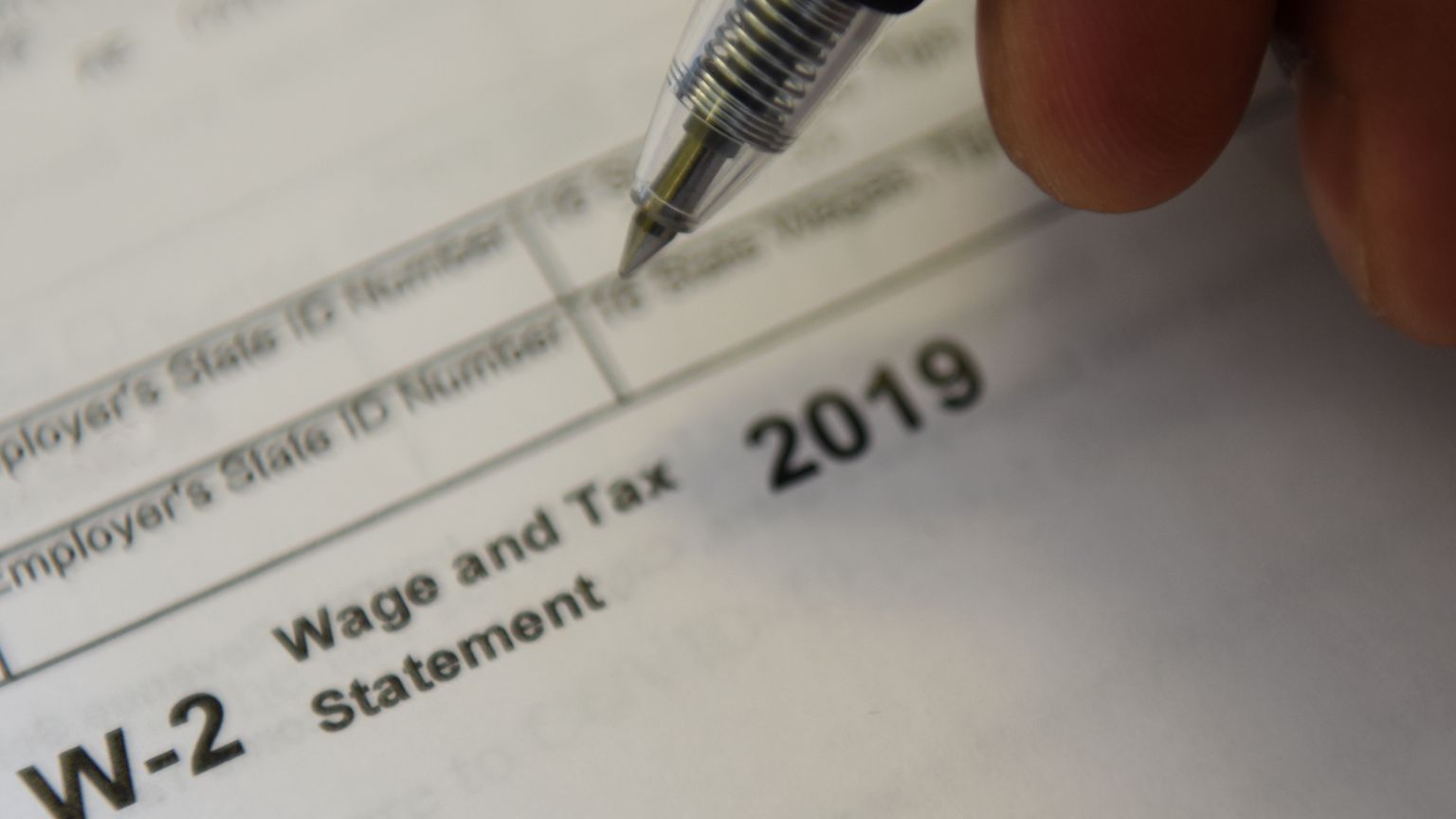 Close-up of a hand holding a pen over a W-2 Wage and Tax Statement form