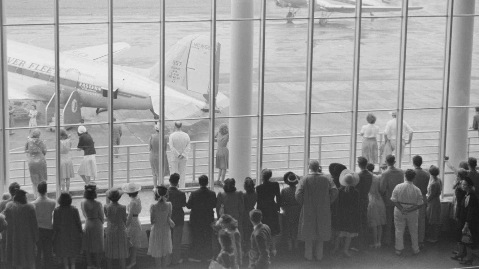 A 1941 black-and-white photo of travelers watching an Eastern Air Lines DC-3 through the tall windows of the waiting room at Washington National Airport