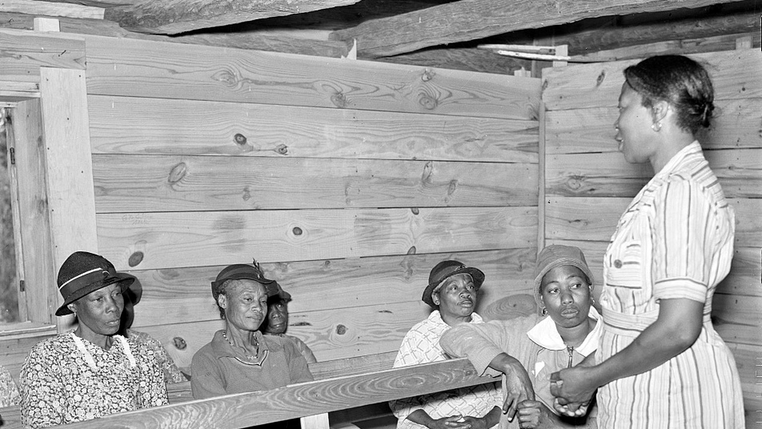 Adult reading and writing class in Gee&rsquo;s Bend, Alabama, 1939: a teacher stands talking to a row of seated adult students