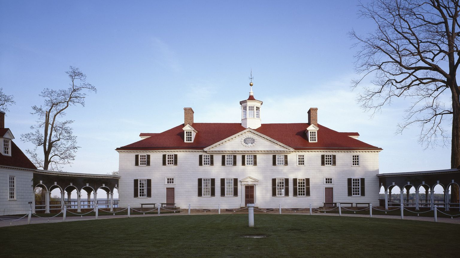 George Washington’s white Mount Vernon mansion with its red roof and cupola, seen across the green bowling lawn under a blue sky