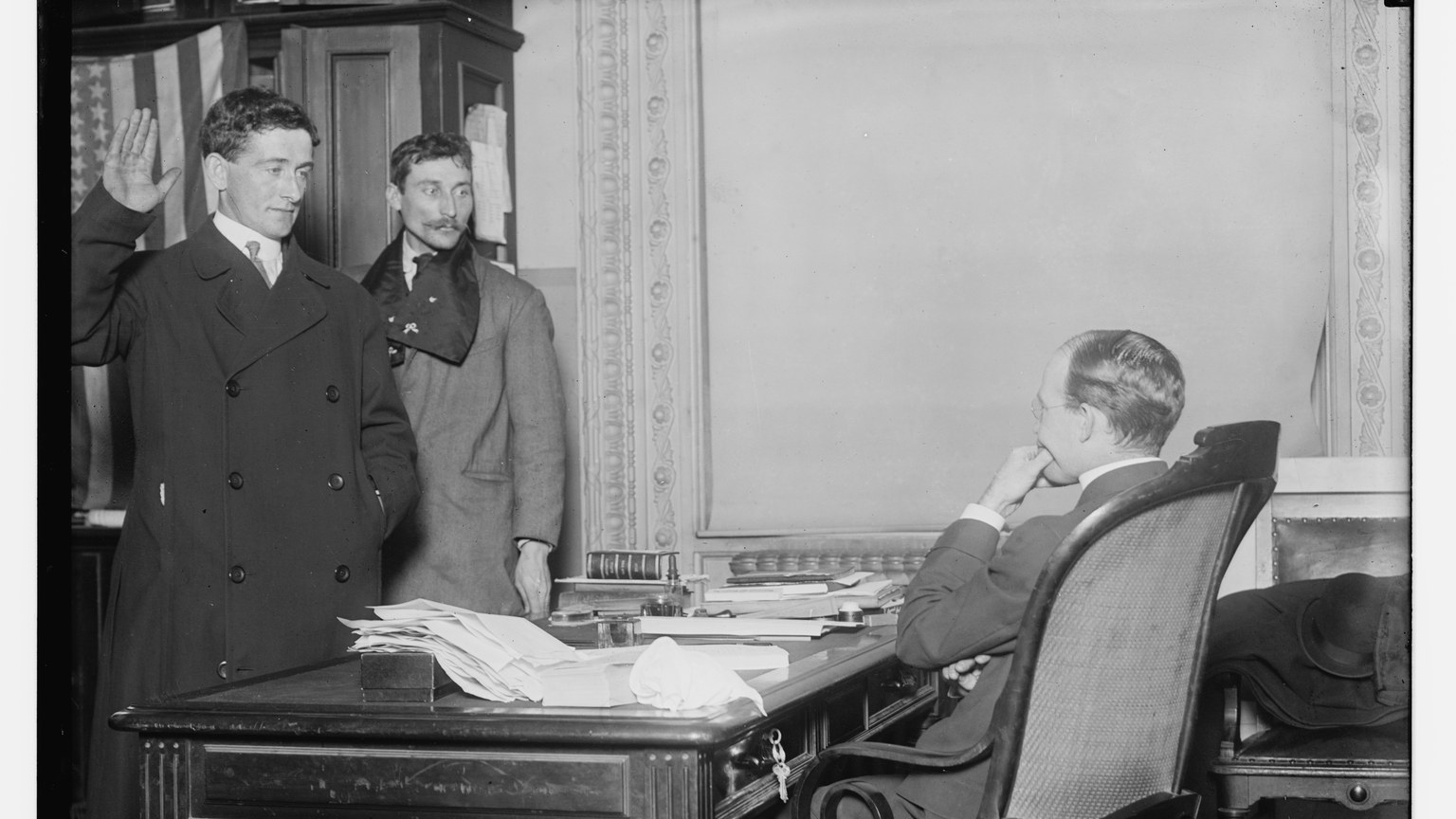 Historic photograph of a new citizen raising a right hand while being sworn in before an official at a desk